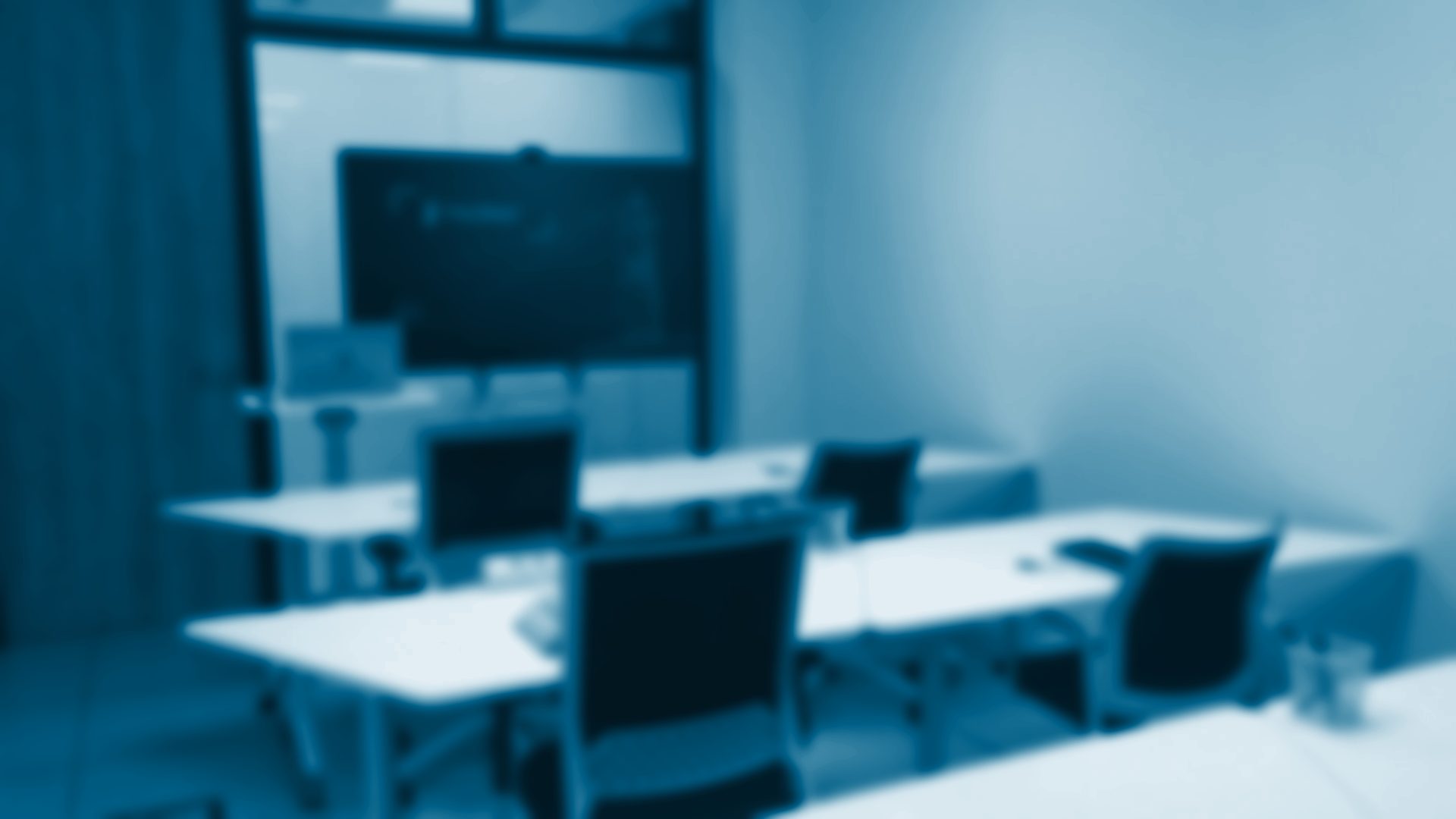 Aula con mesas blancas, sillas y una pantalla grande al fondo