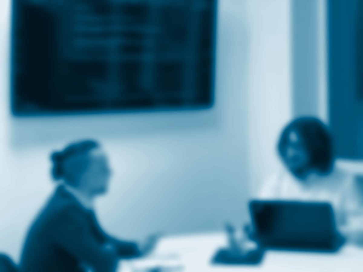 Dos profesionales conversan en una mesa redonda, con código en la pantalla del fondo